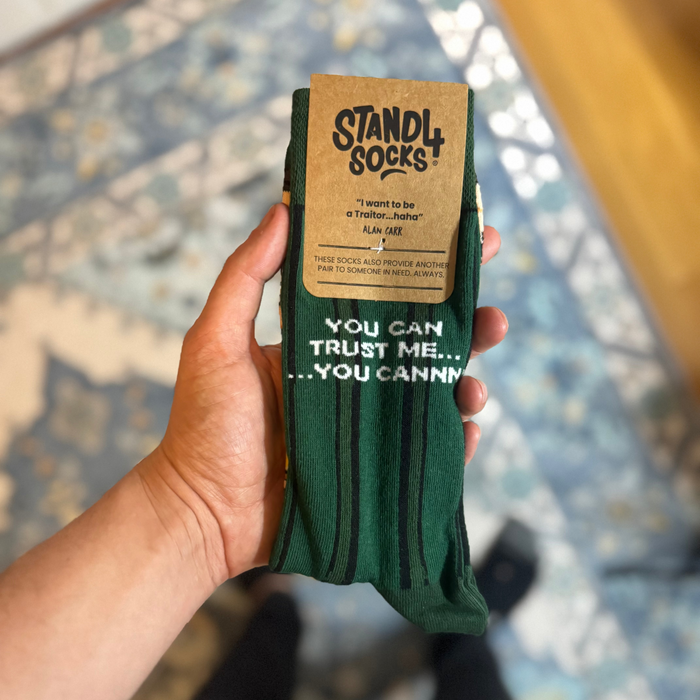 Green Alan Carr Traitors sock in packaging held outdoors | Stand4 Socks buy one, give one to someone homeless