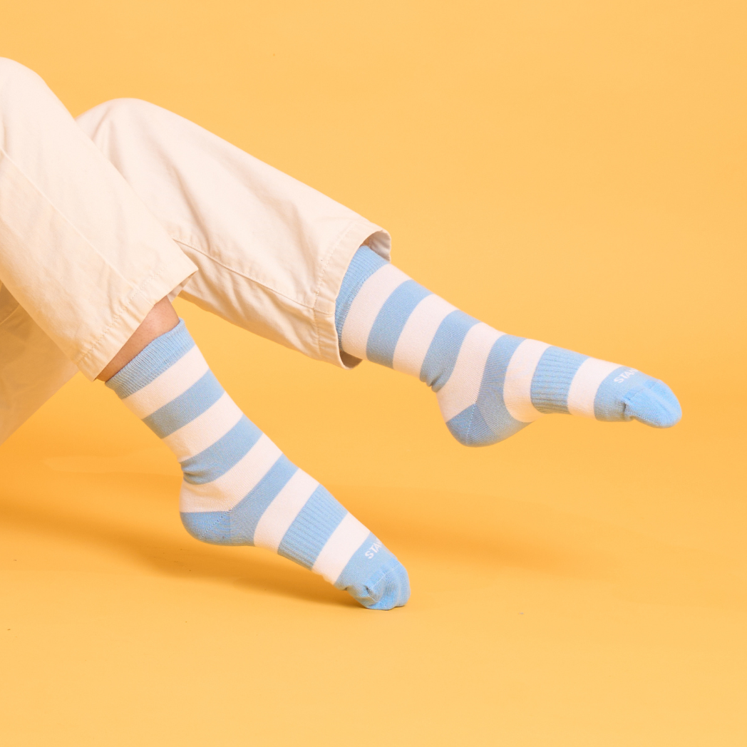 Baby blue striped socks worn with white trousers against a yellow background | Stand4 Socks