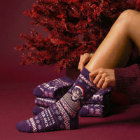 Purple Christmas Theroux socks styled beside a seated model and red festive decorations | Stand4 Socks