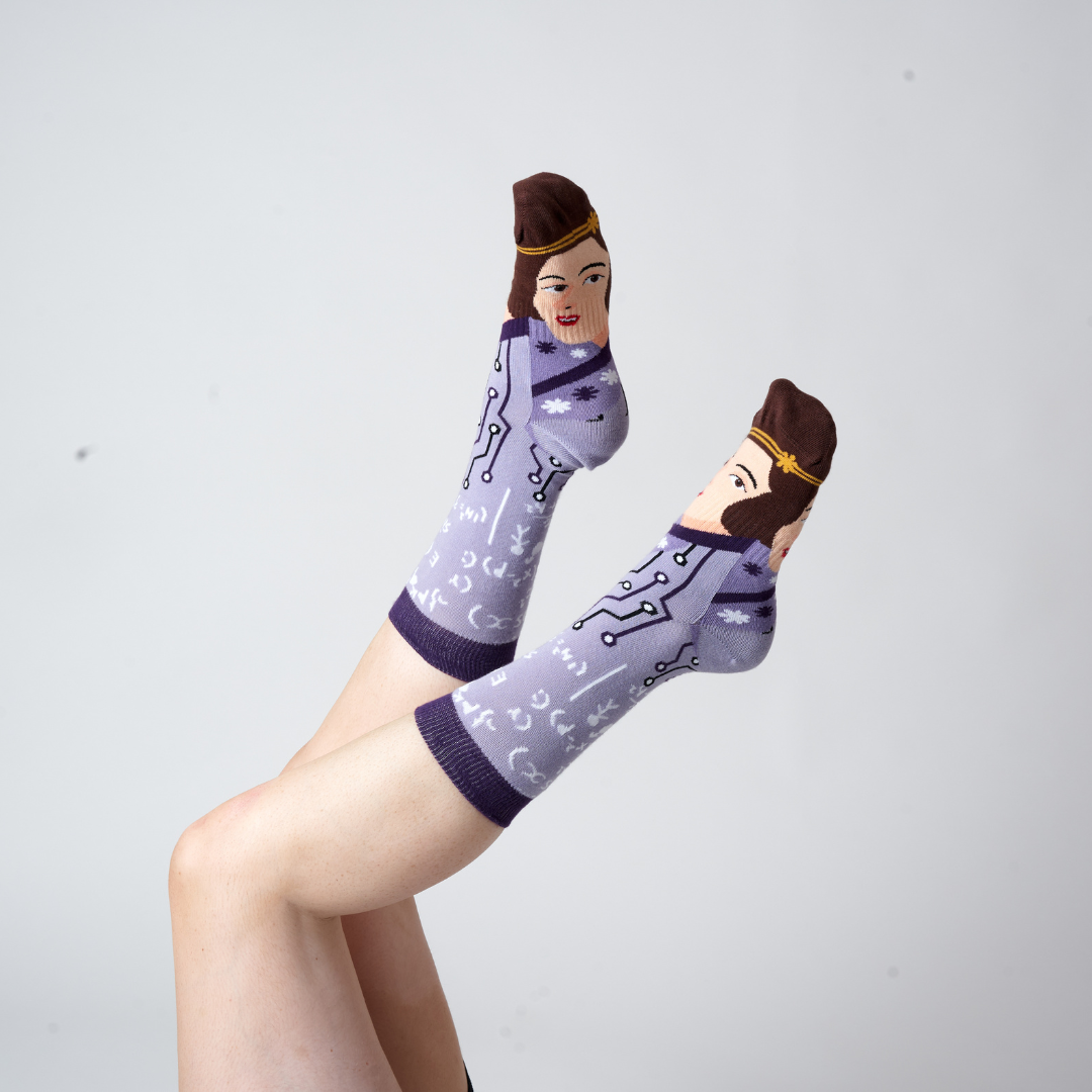 Purple Ada Lovelace crew socks worn on raised feet against a grey studio background | Stand4 Socks