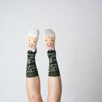 Green Albert Einstein portrait socks worn on raised feet against a grey background | Stand4 Socks