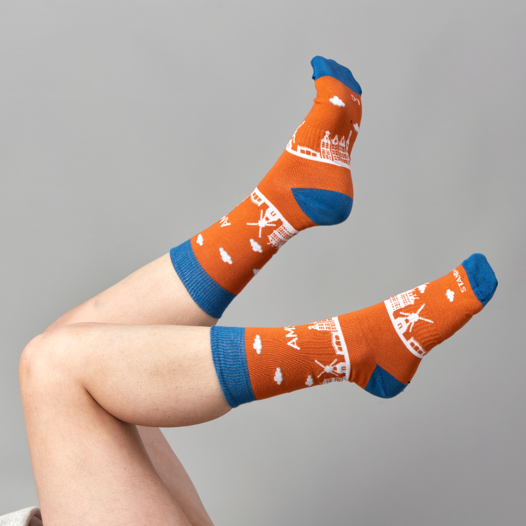 Orange Amsterdam Skyline socks worn on raised feet against a grey background | Stand4 Socks