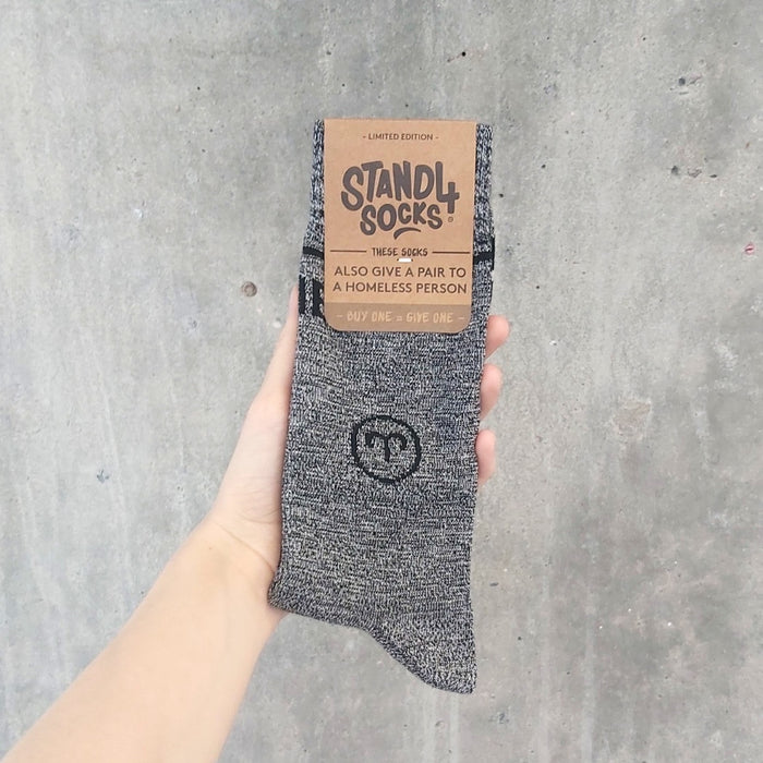 Grey Aries Zodiac sock in packaging held against a concrete background | Stand4 Socks buy one, give one to someone homeless