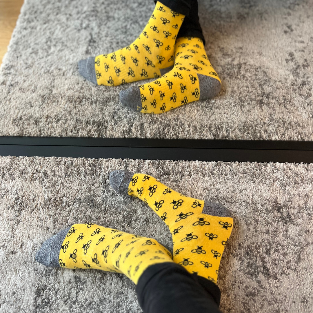 Yellow bee-pattern socks worn on both feet in front of a mirror | Stand4 Socks