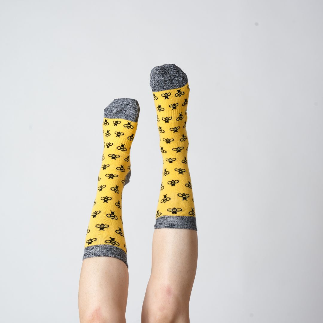 Yellow bee-pattern socks worn on raised feet against a grey background | Stand4 Socks