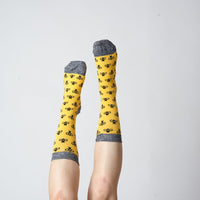 Yellow bee-pattern socks worn on raised feet against a grey background | Stand4 Socks