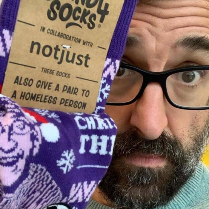 Louis Theroux holding a purple Christmas Theroux sock beside his face | Stand4 Socks
